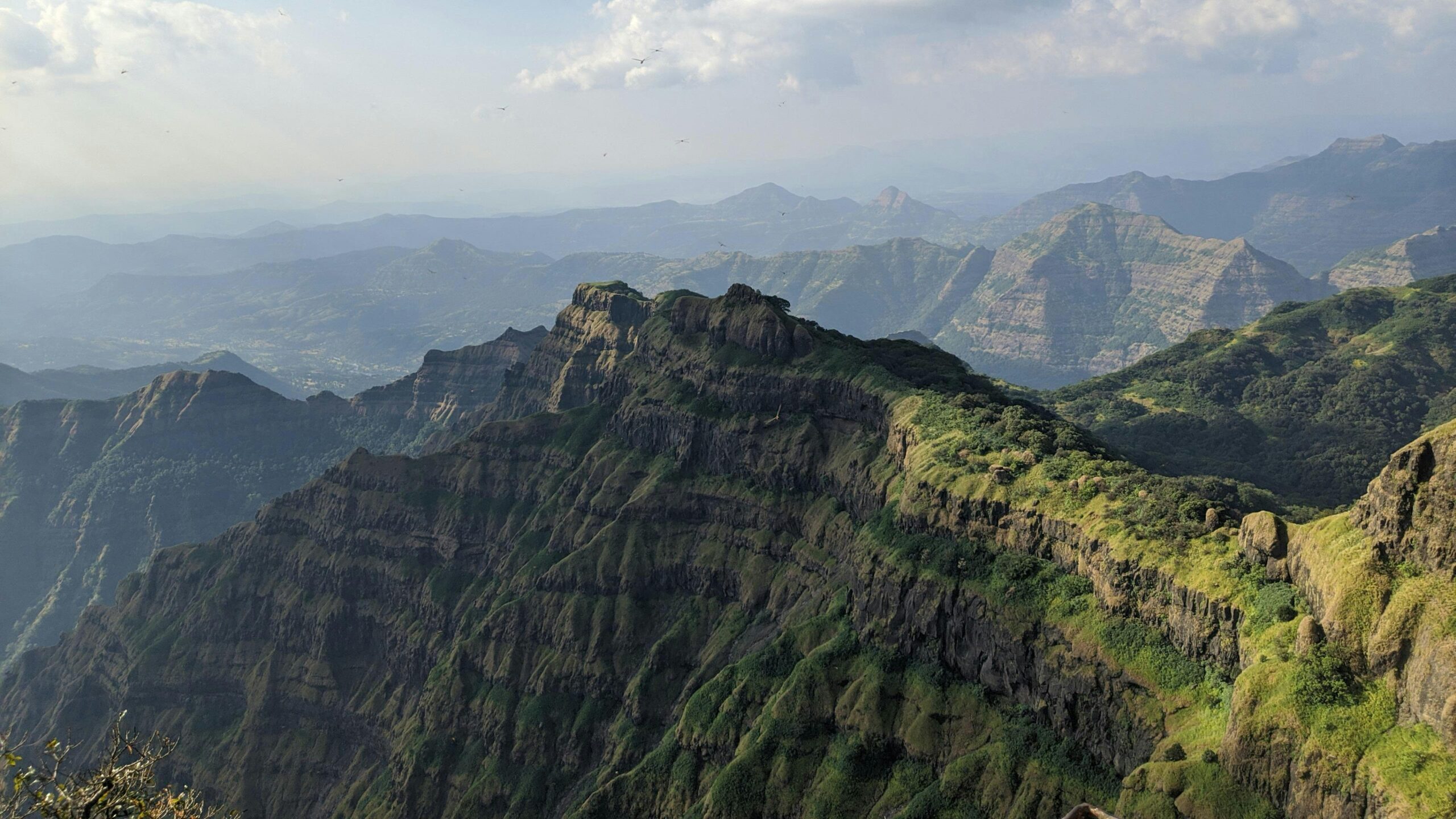 Panoramic mountain landscape from Harishchandragad fort trek in Maharashtra, featuring dramatic cliffs, green valleys, and Sahyadri mountain ranges
